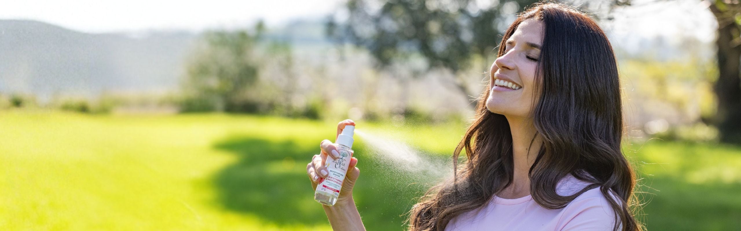 femme souriante qui vaporise de la brume parfumée énergisante